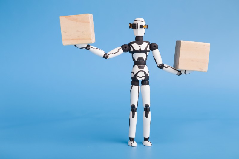 Ein computergezeichneter Roboter vor blauem Hintergrund hält 2 Boxen in den Händen